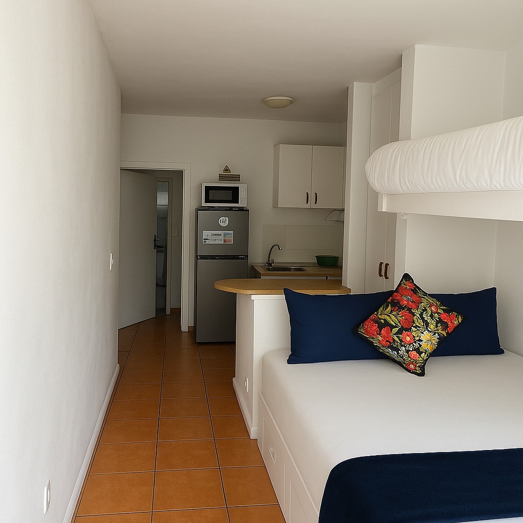 Studio apartment with bed with navy pillows, bunk bed above, kitchenette, terracotta tile floor