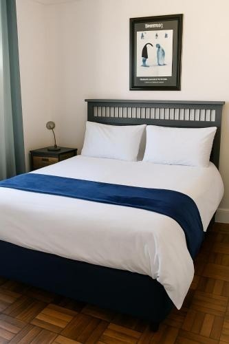 Bedroom with white sheets, blue runner, black wooden headboard, nightstand with lamp, framed print