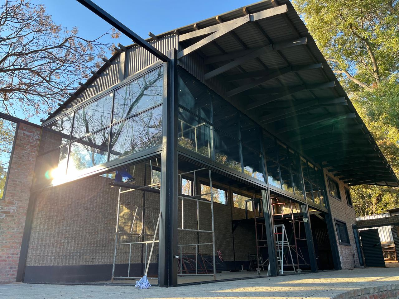 Modern industrial-style building with large black steel framing, extensive glass windows, metal pergola roof