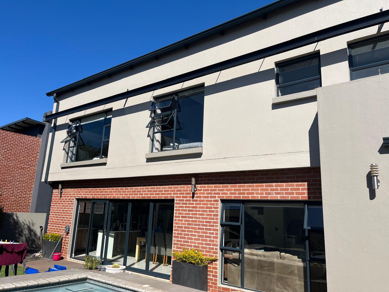 Modern two-story residential building with brick base, large glass doors, cream upper level, horizontal windows, patio with pool
