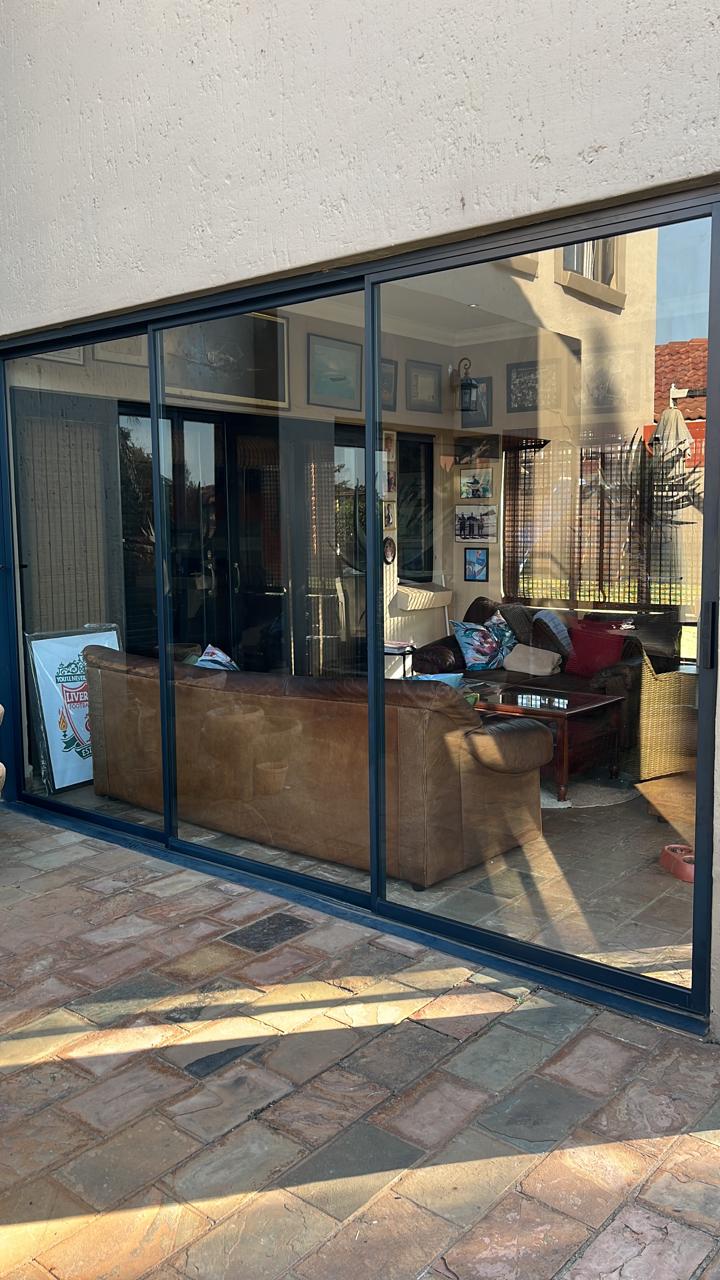 Modern sunroom or conservatory with large glass sliding doors and windows, brown leather furniture, patio