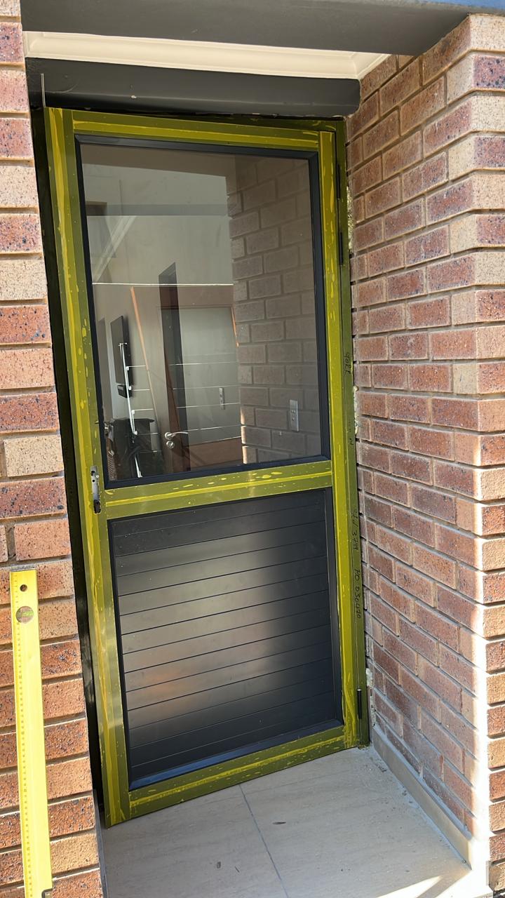 Bright yellow-green modern door with black horizontal slats and glass panel, brick entryway