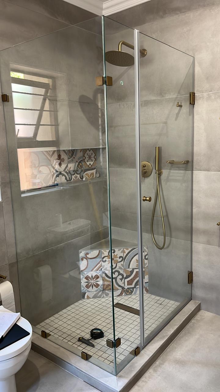 Modern bathroom with spacious glass-enclosed walk-in shower, bronze hardware, decorative tile accents, rainfall showerhead