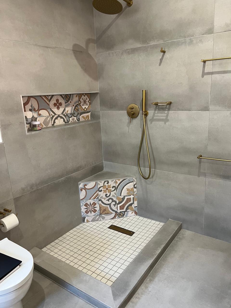 Modern bathroom shower with large format grey tiles, brass fixtures, rainfall showerhead, walk-in layout