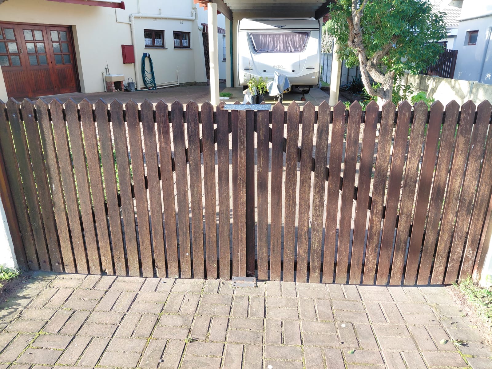 Wooden picket fence and carport sheltering a camper trailer