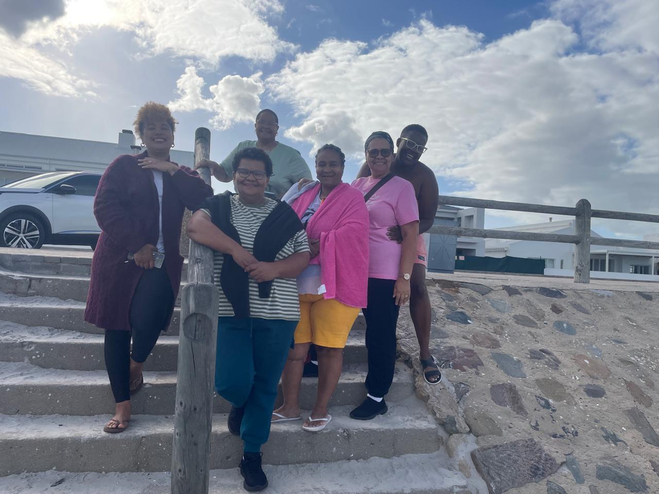 Group of six friends posing on a sunny beach during a retreat gathering