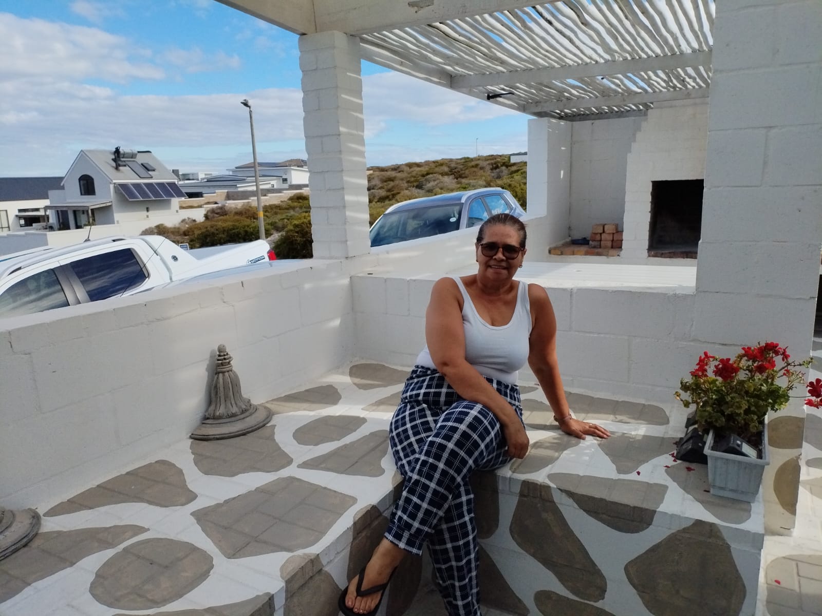 Woman posing on a white rooftop terrace with patterned flooring, pergola, and coastal landscape views
