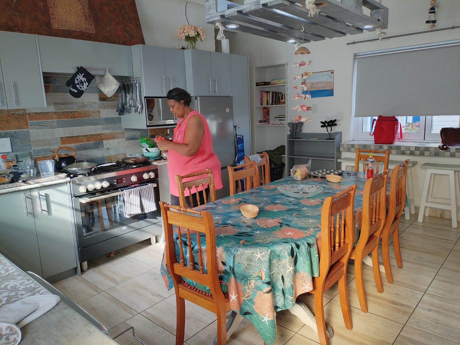 Woman cooking in a modern light blue coastal kitchen near a dining table with patterned tablecloth