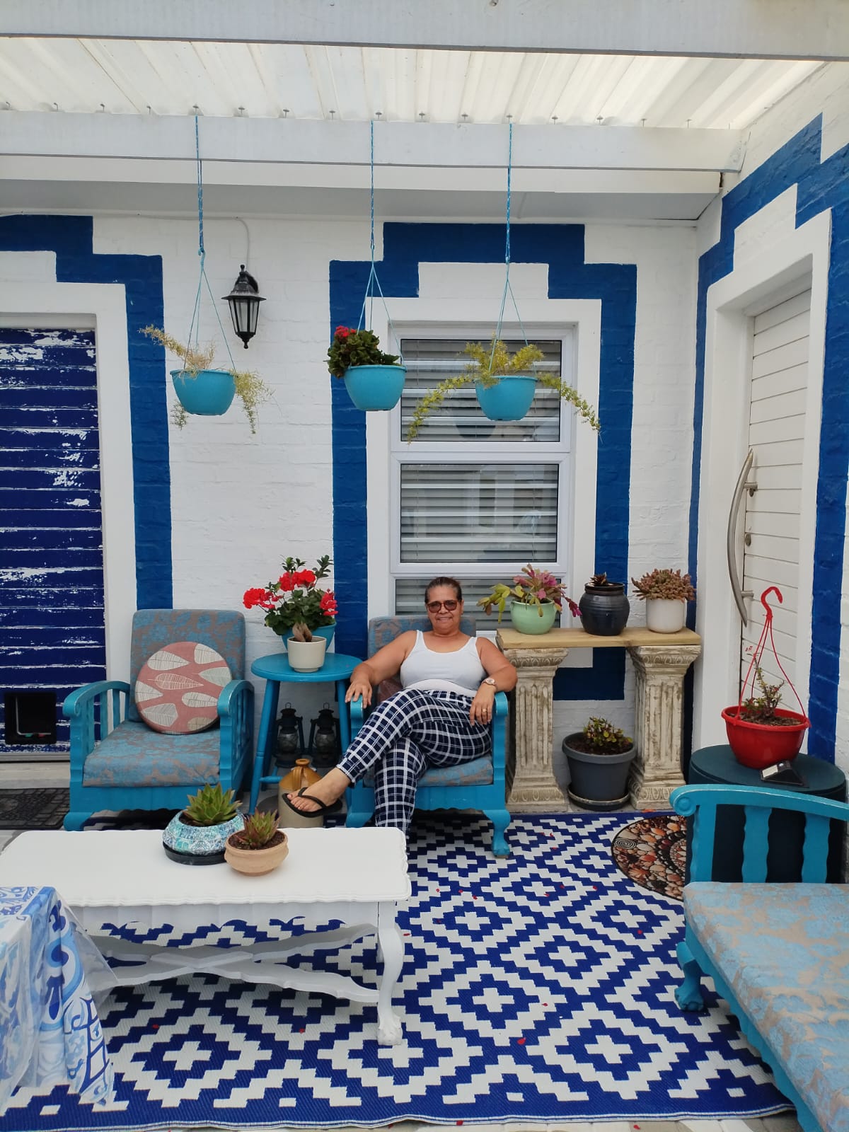 Woman on a turquoise chair in a vibrant blue and white patio with hanging planters