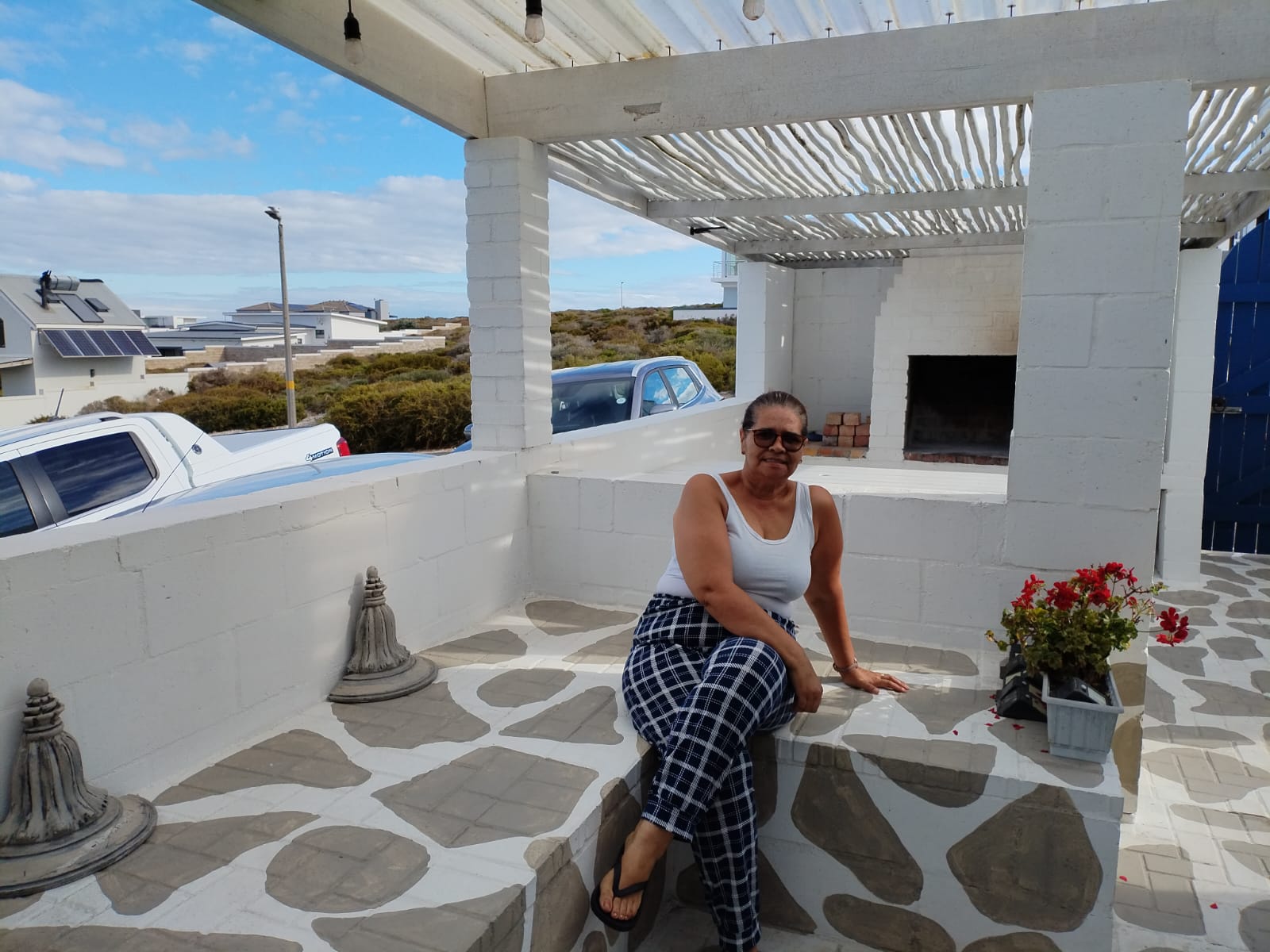 Woman sitting on a stone bench in a modern white courtyard with geometric tile flooring and pergola