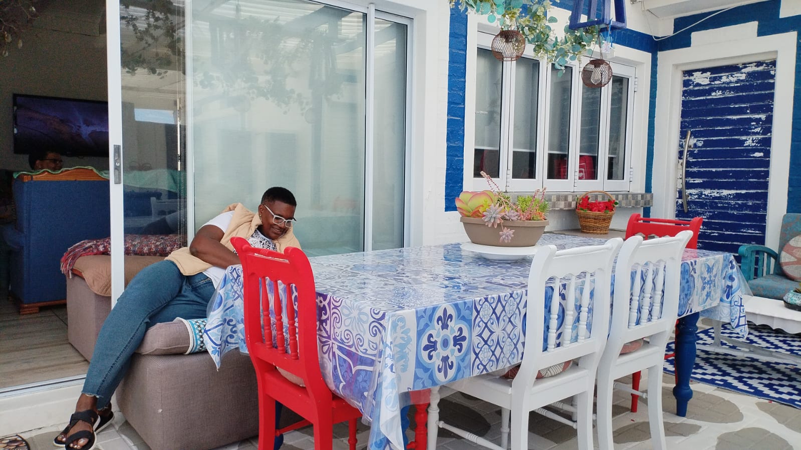 Man sitting at a dining table in a blue and white coastal interior with red chairs and potted plants