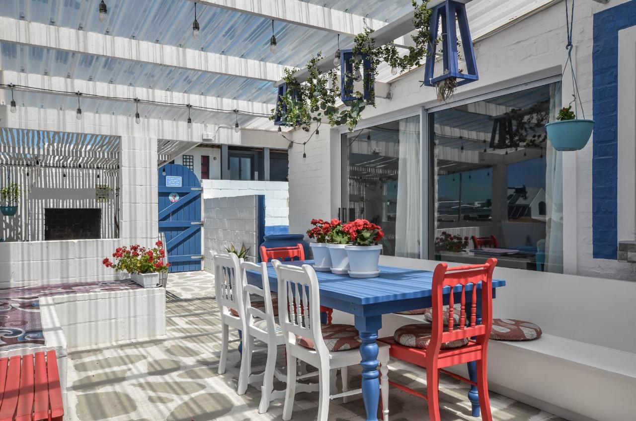 Coastal outdoor patio with blue and white dining table, red chairs, and red geraniums