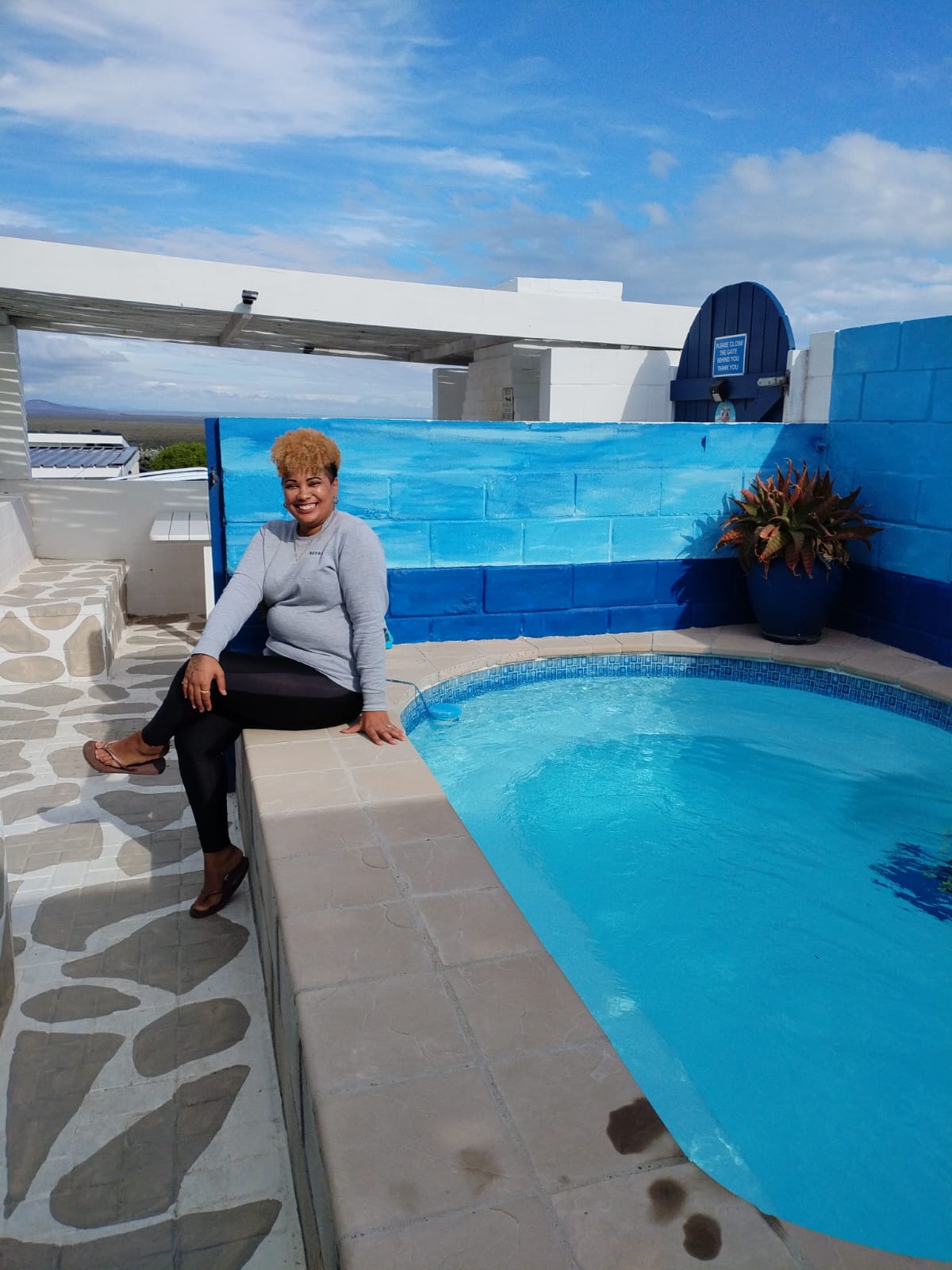 Woman sitting at the edge of a bright blue swimming pool on a white rooftop terrace with mountain views