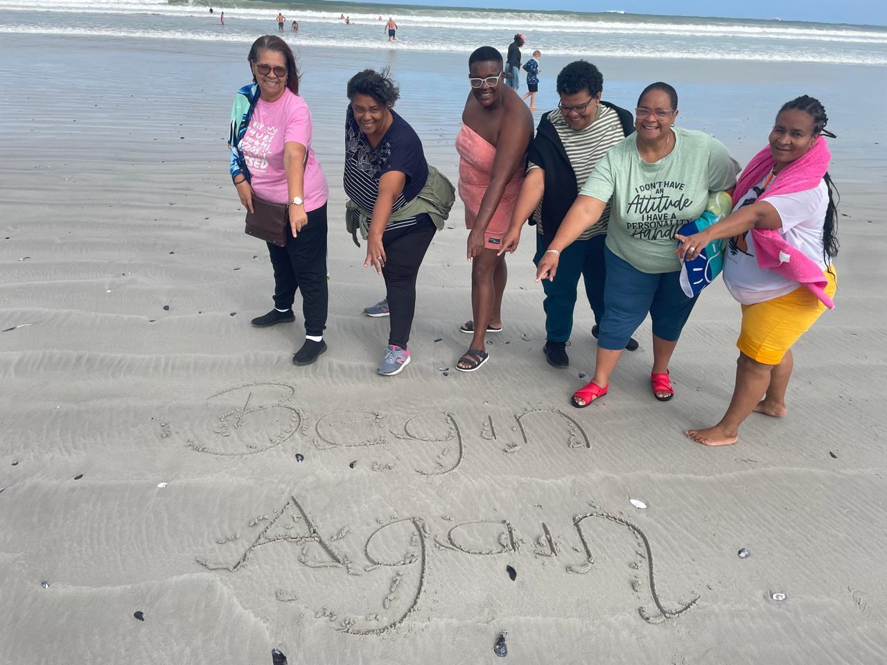 Group of friends posing together on the beach with names written in the sand