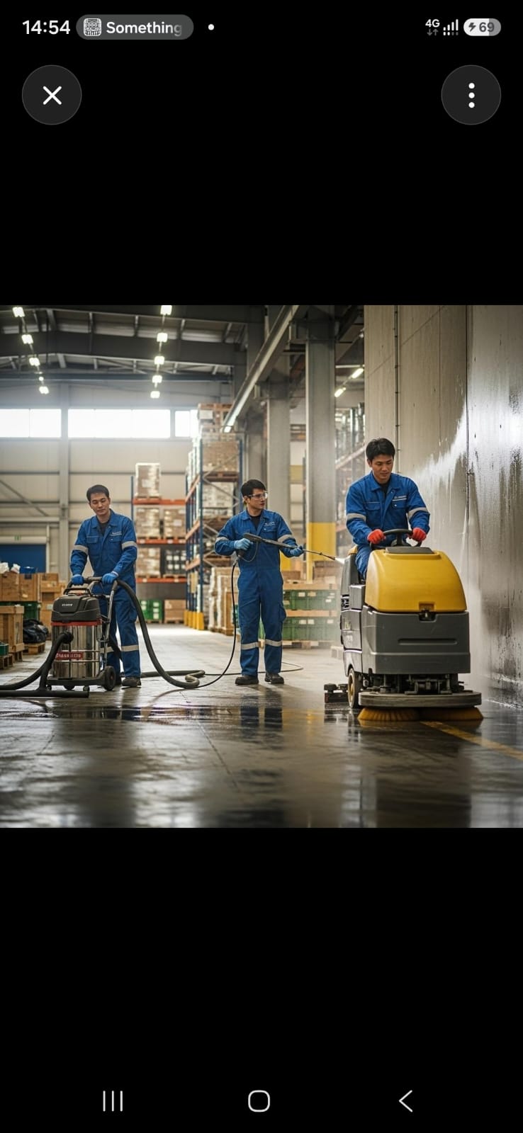 Three workers in blue uniforms cleaning a large warehouse floor with industrial equipment