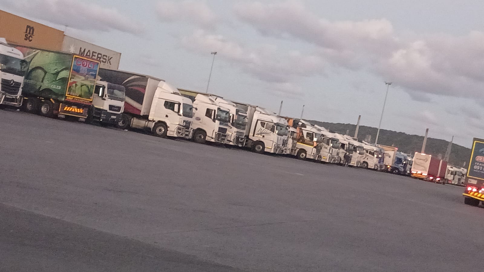 Line of white commercial trucks and shipping containers at a logistics and freight facility