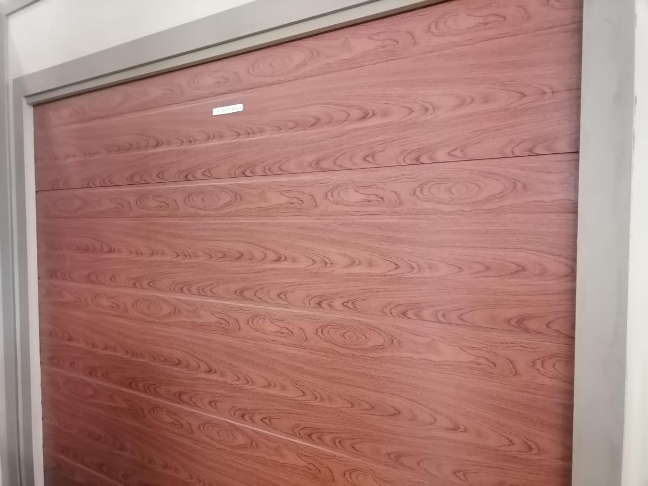 Modern garage door with wood grain finish in mauve-pink featuring horizontal panel sections and a small upper window