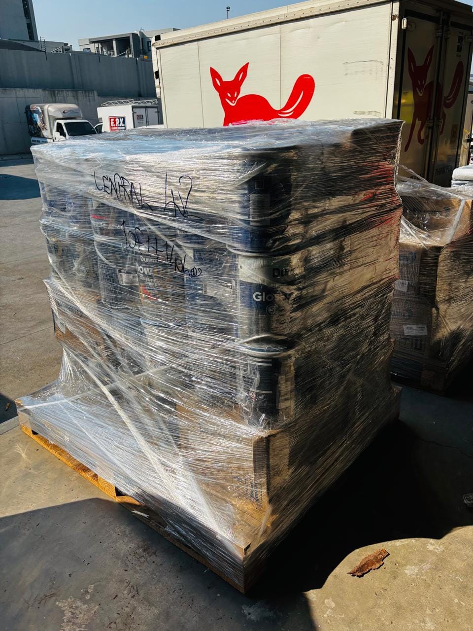Large pallet of wrapped industrial supplies in a yard with shipping container in background