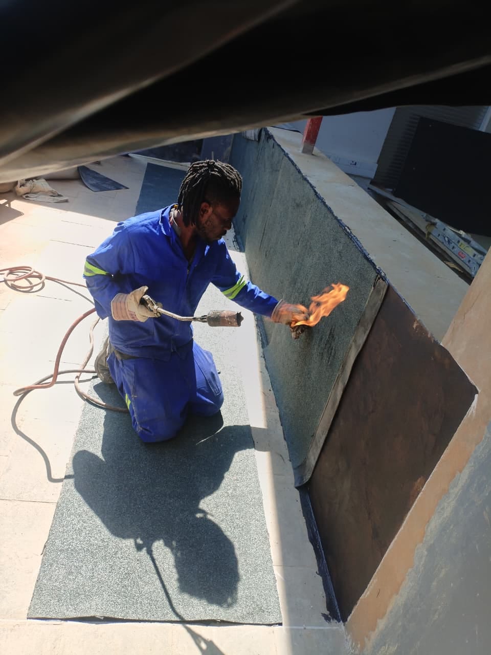 Worker in blue uniform applying waterproof coating with blowtorch on rooftop