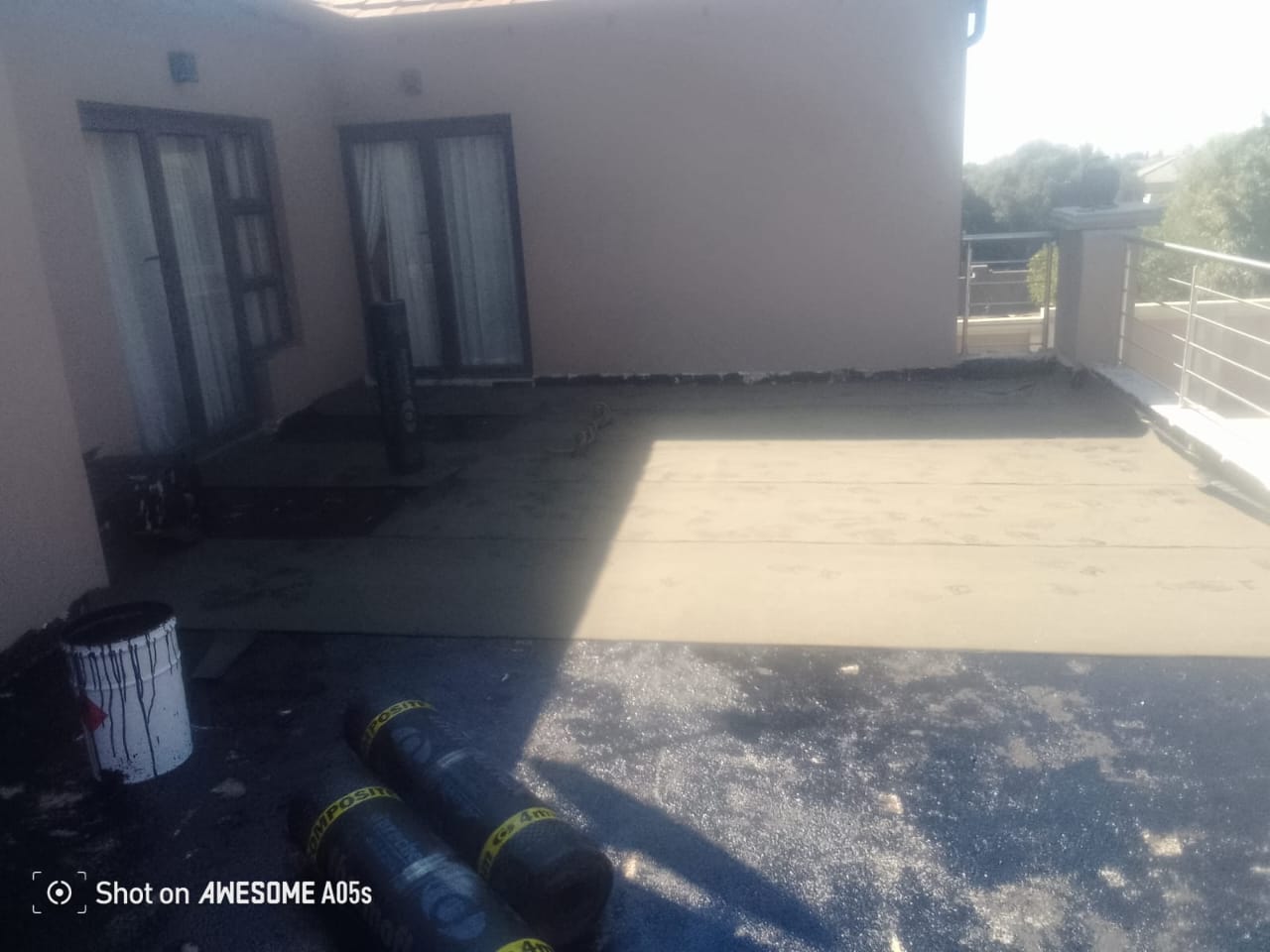 Residential rooftop terrace with white walls, glass doors, metal railing, and rolled waterproofing membrane
