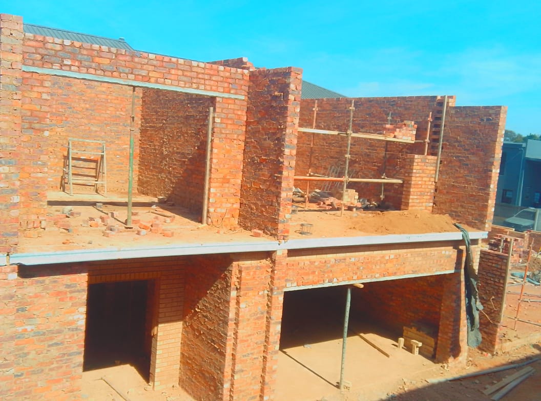 Brick residential building under construction with scaffolding and roof beams against blue sky