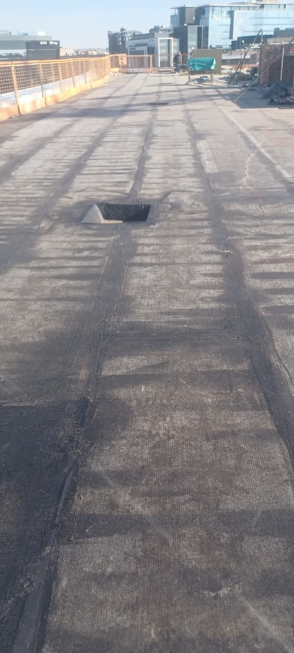 Rooftop with worn rubber membrane and metal fencing overlooking city skyline