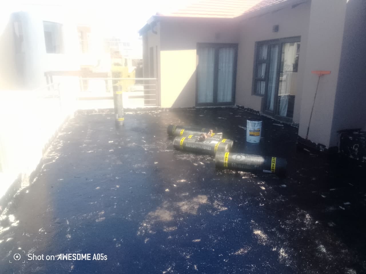 Rooftop terrace under construction with rolled tar paper and bucket beside sliding glass doors