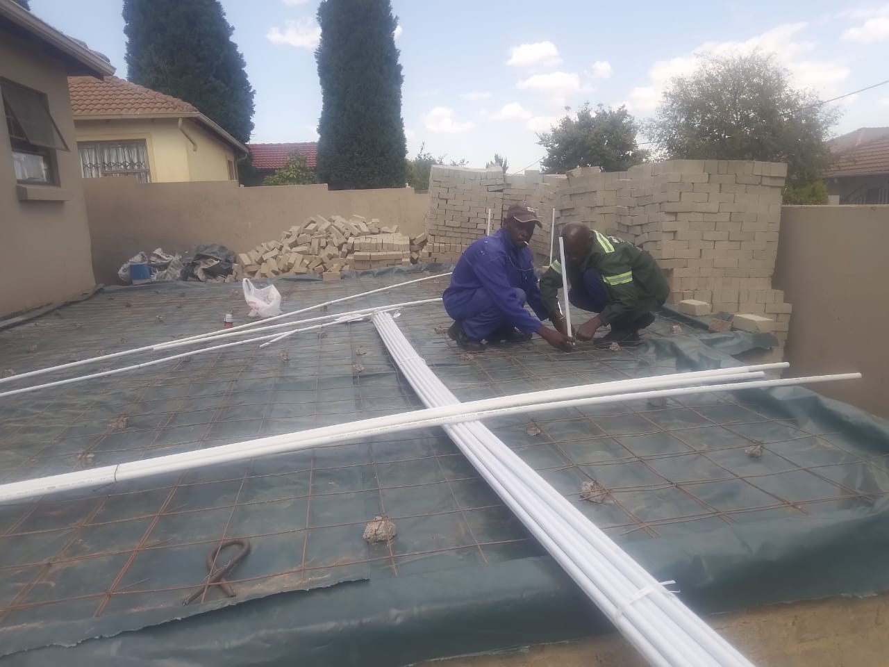 Workers installing metal framing and waterproofing membranes on foundation