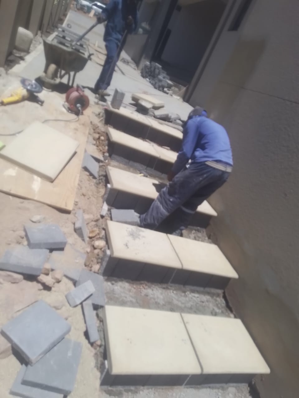 Workers laying large paving stones on exterior ground surface