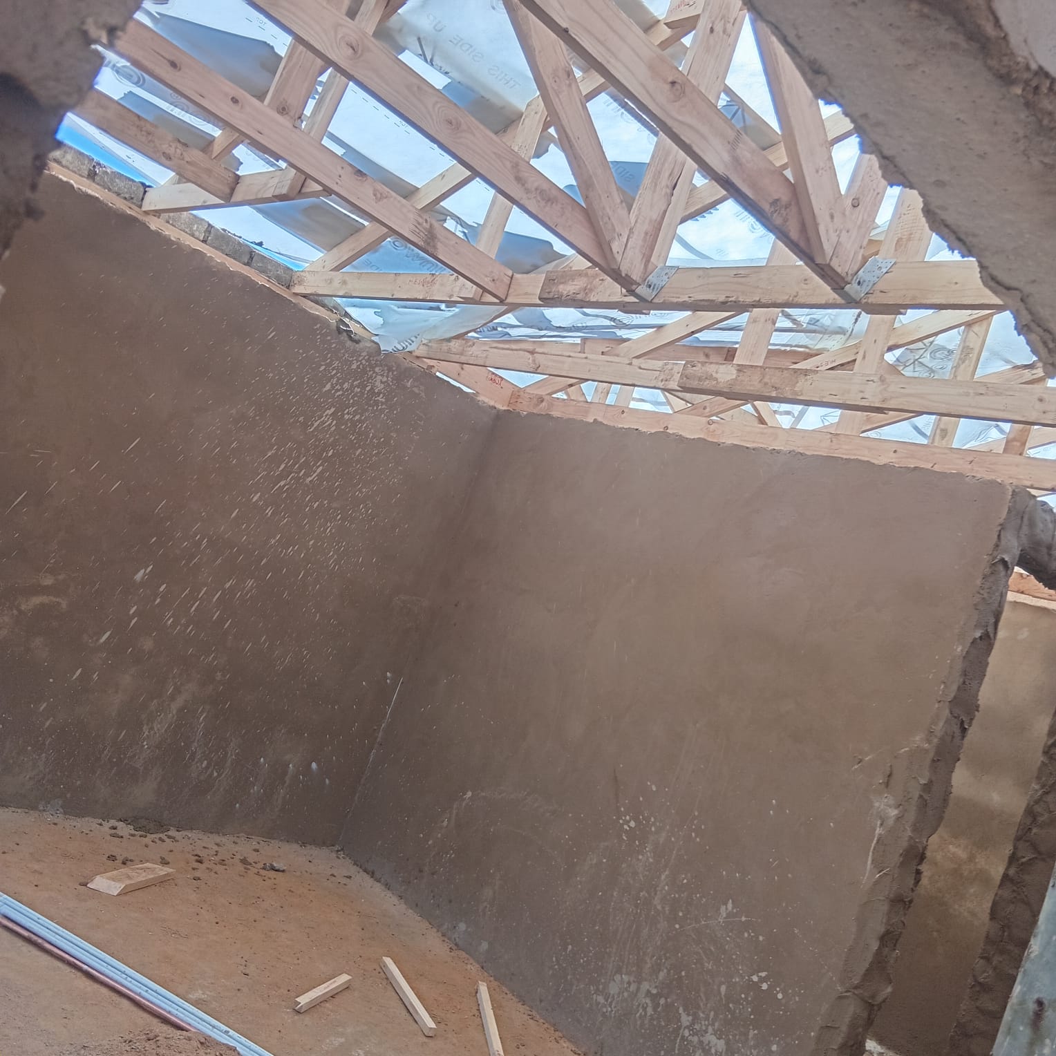 Bare concrete walls with exposed wooden roof framing against blue sky