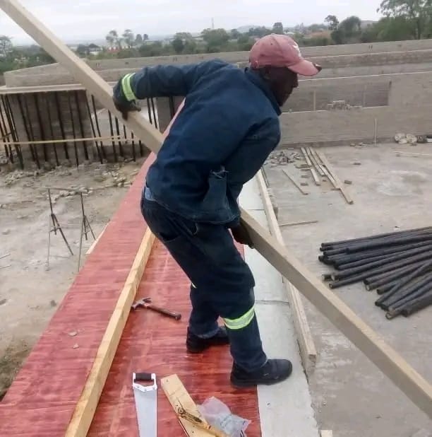 Worker in safety gear installing red roofing on concrete structure