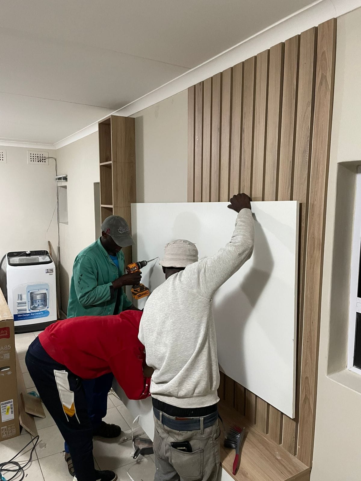 Two workers installing white wall panels against wooden slat wall