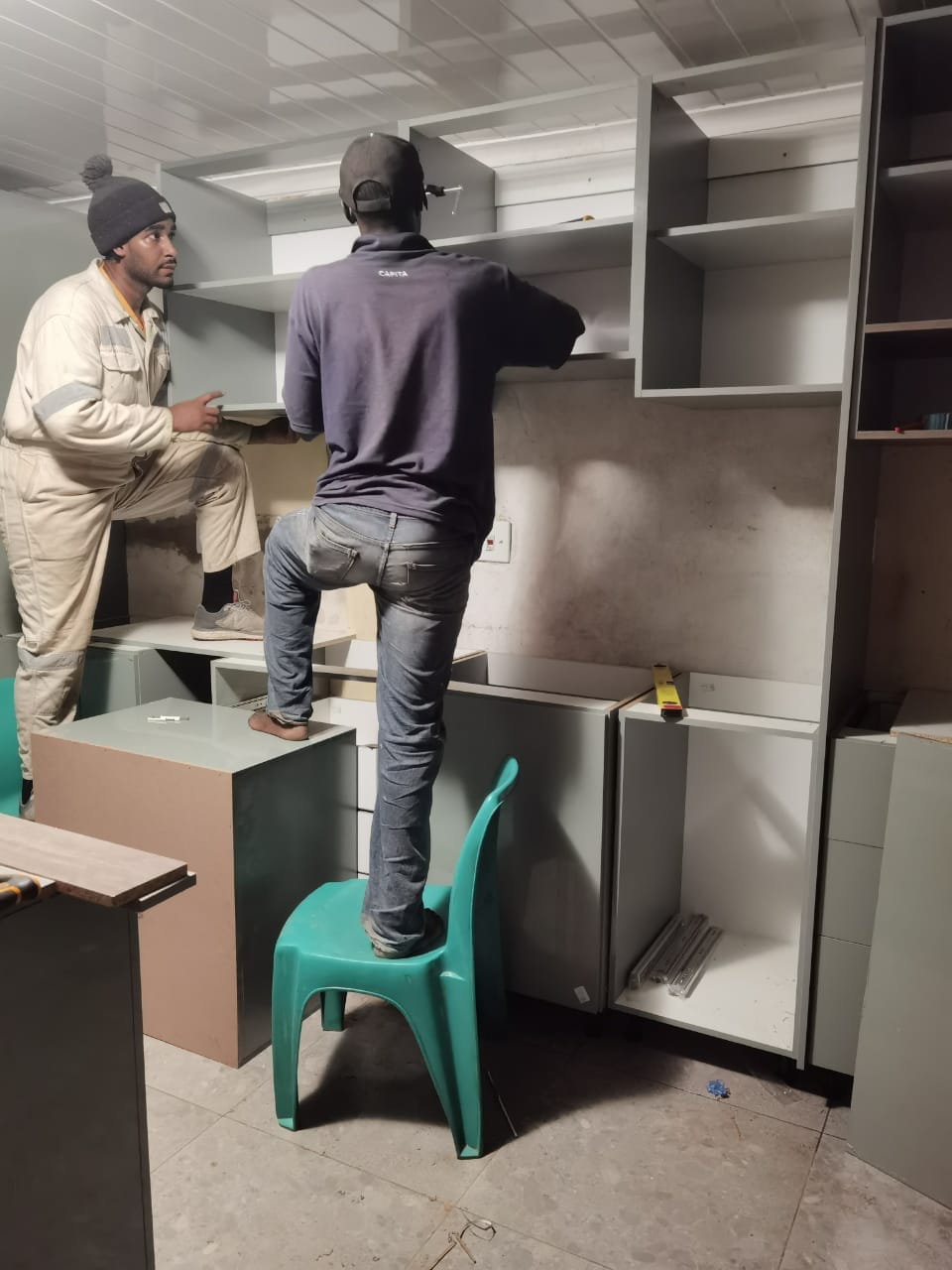 Two workers installing built-in shelving in a room under construction