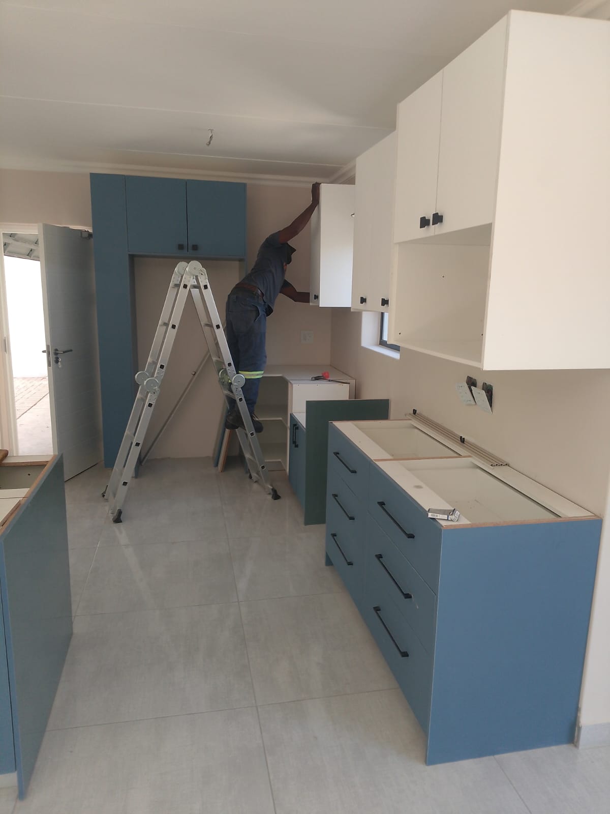 Worker installing modern blue and white kitchen cabinets in renovated space