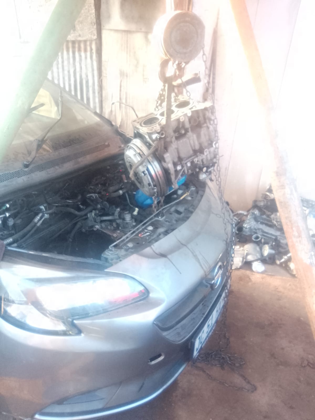 Car engine open under a covered garage showing internal mechanical components