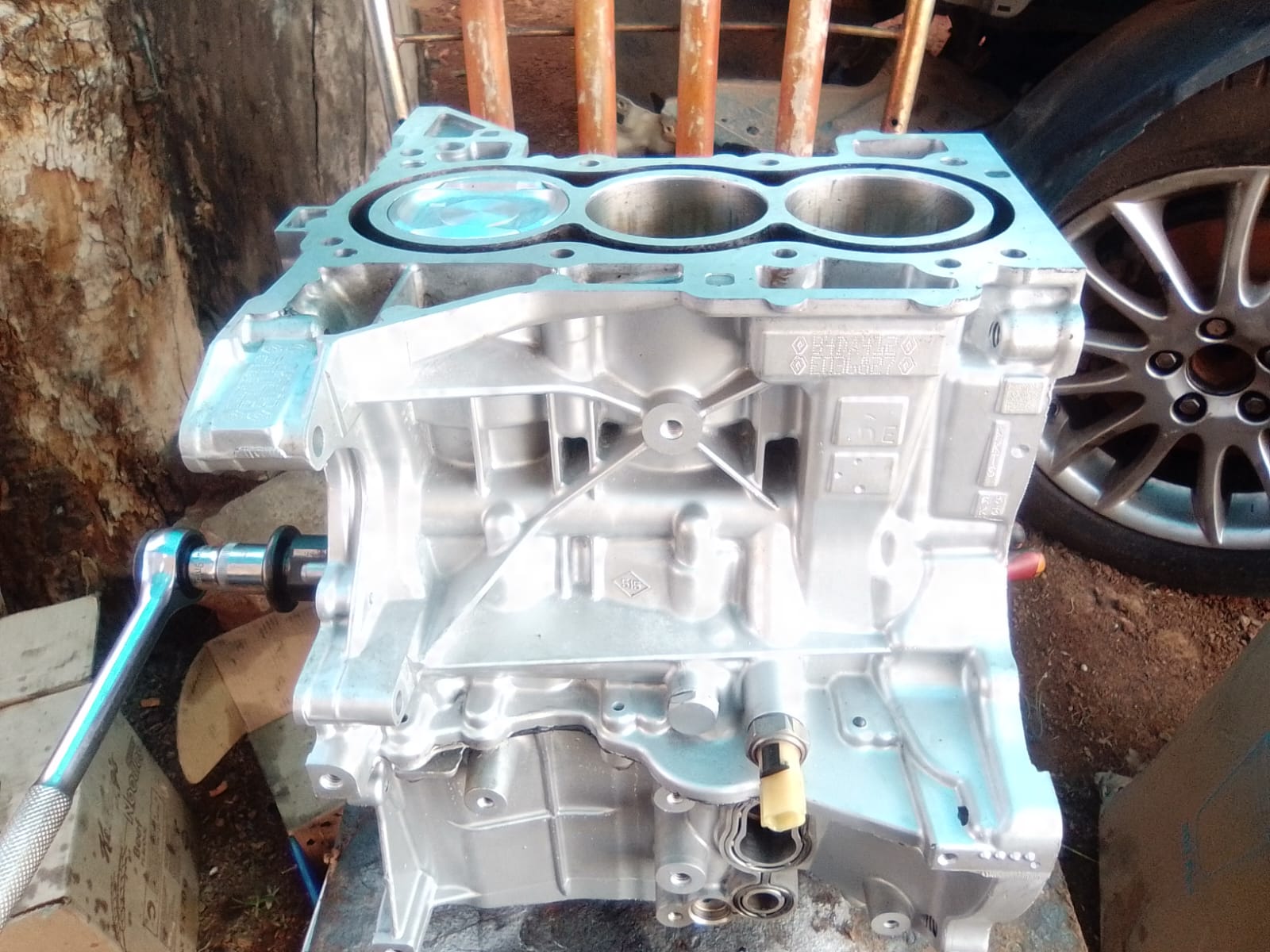 Freshly machined three-cylinder engine block with blue gasket surface on workbench