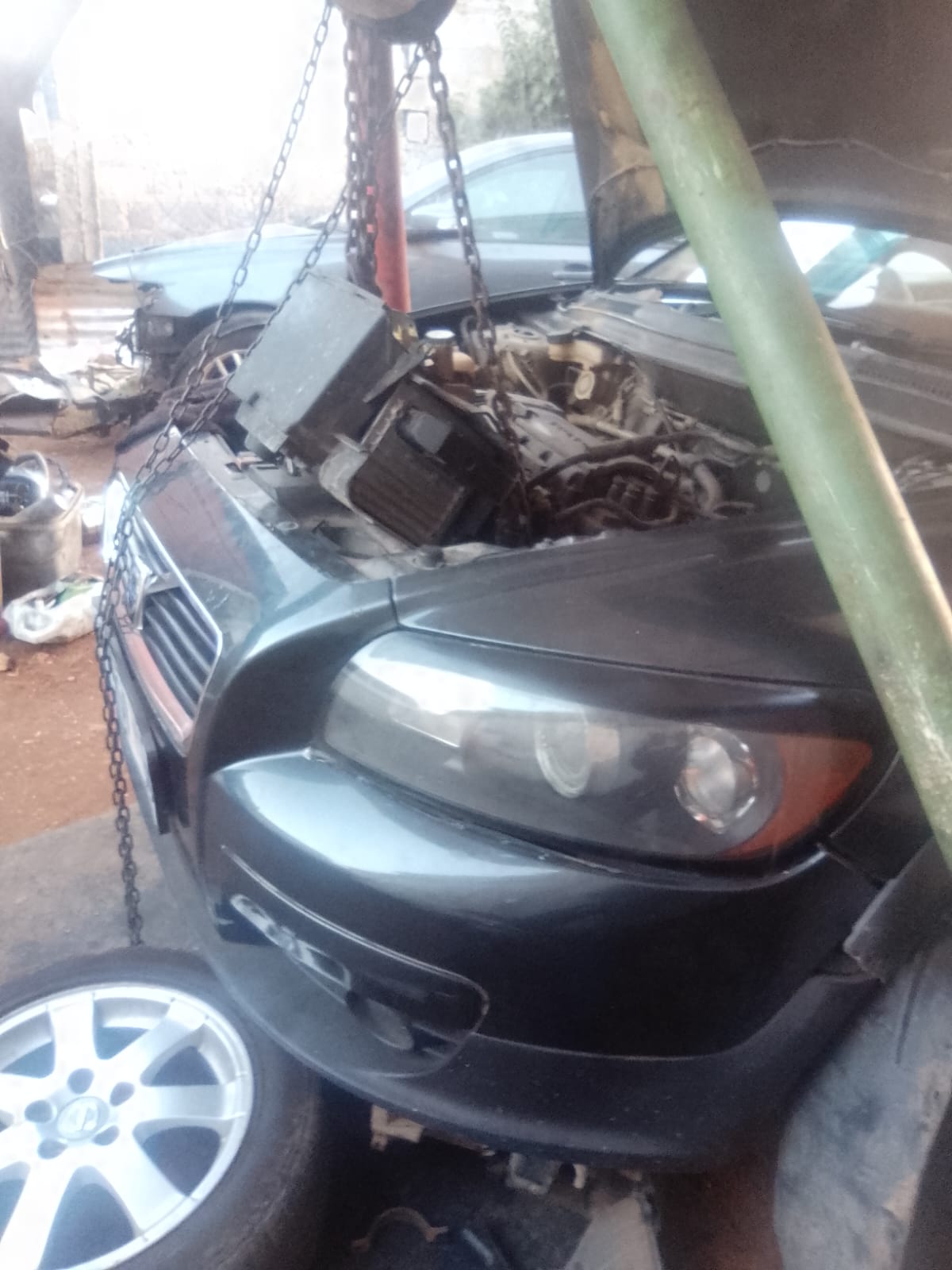Black car being lifted by chain hoist with exposed engine compartment
