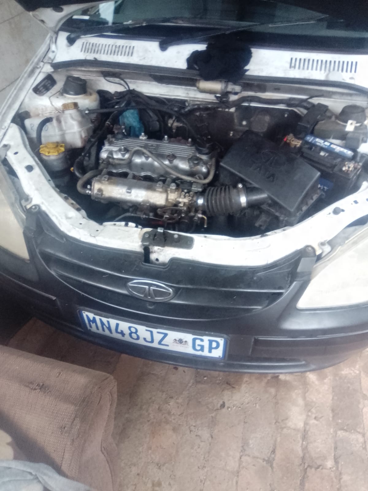 Open car hood showing engine compartment of a white Tata vehicle