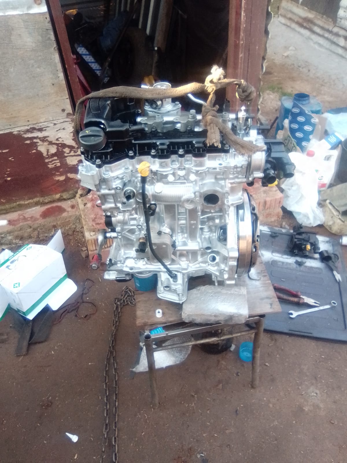 Disassembled car engine on the ground outside a workshop showing internal components and mechanical parts during a rebuild