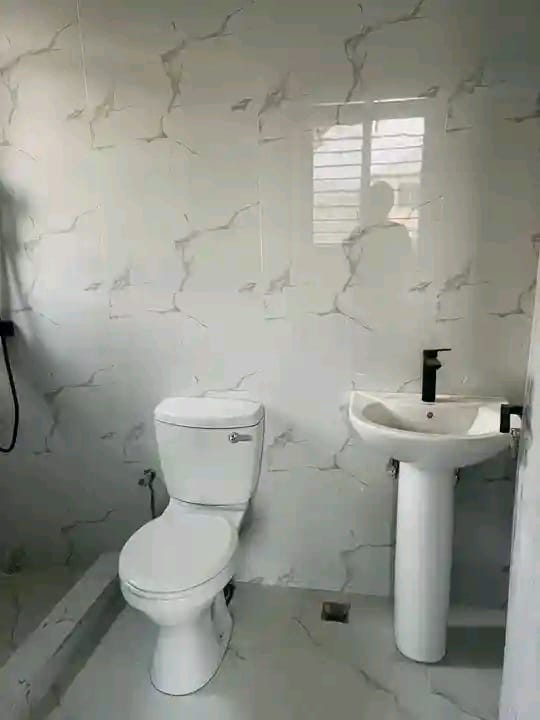 Bathroom with white marble-patterned tiles, toilet and pedestal sink with black faucets, and a shuttered window
