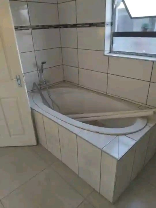 Modern bathroom with curved corner bathtub, shower head, and white tile surround