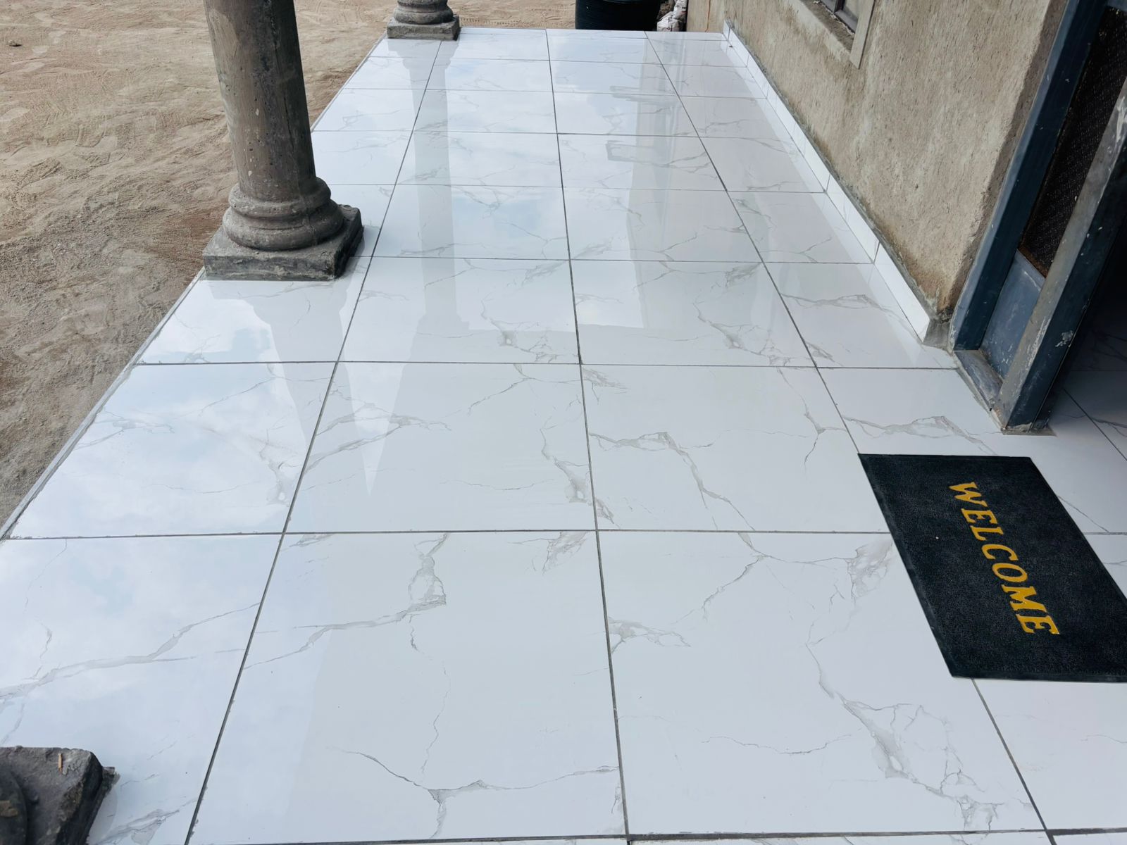 White marble-effect tiled entryway with a black welcome mat and decorative columns