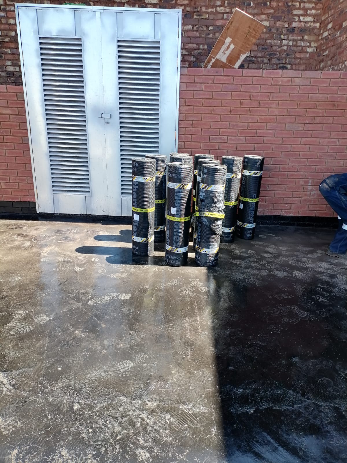 Stacked rolled roofing materials against a brick wall