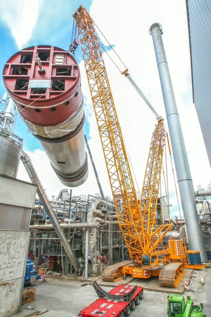 Industrial crane lifting a red cylindrical tank structure