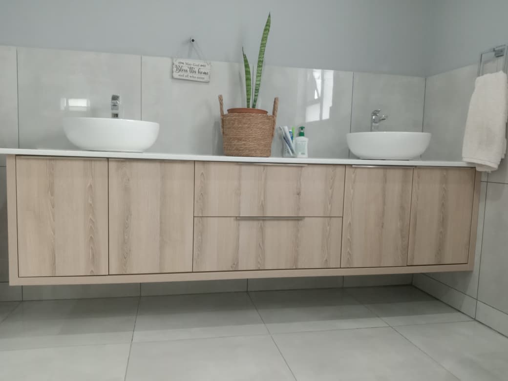 Bathroom vanity with floating light wood cabinetry and white vessel sinks