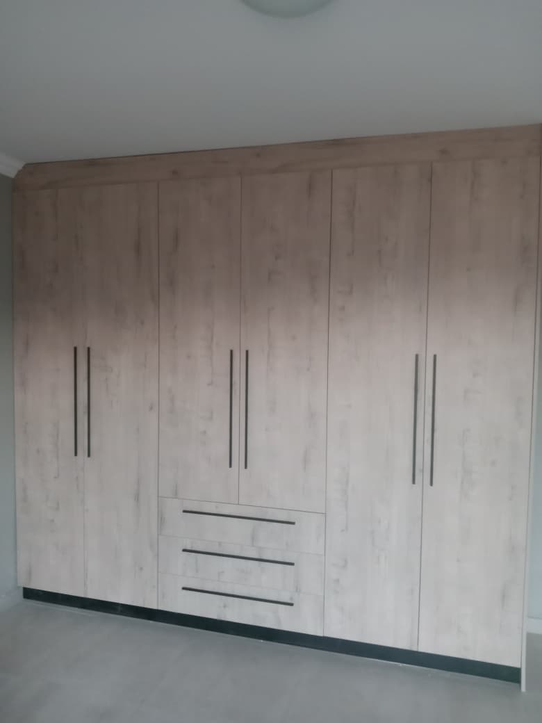 Built-in whitewashed wardrobe with black metal handles and lower drawers