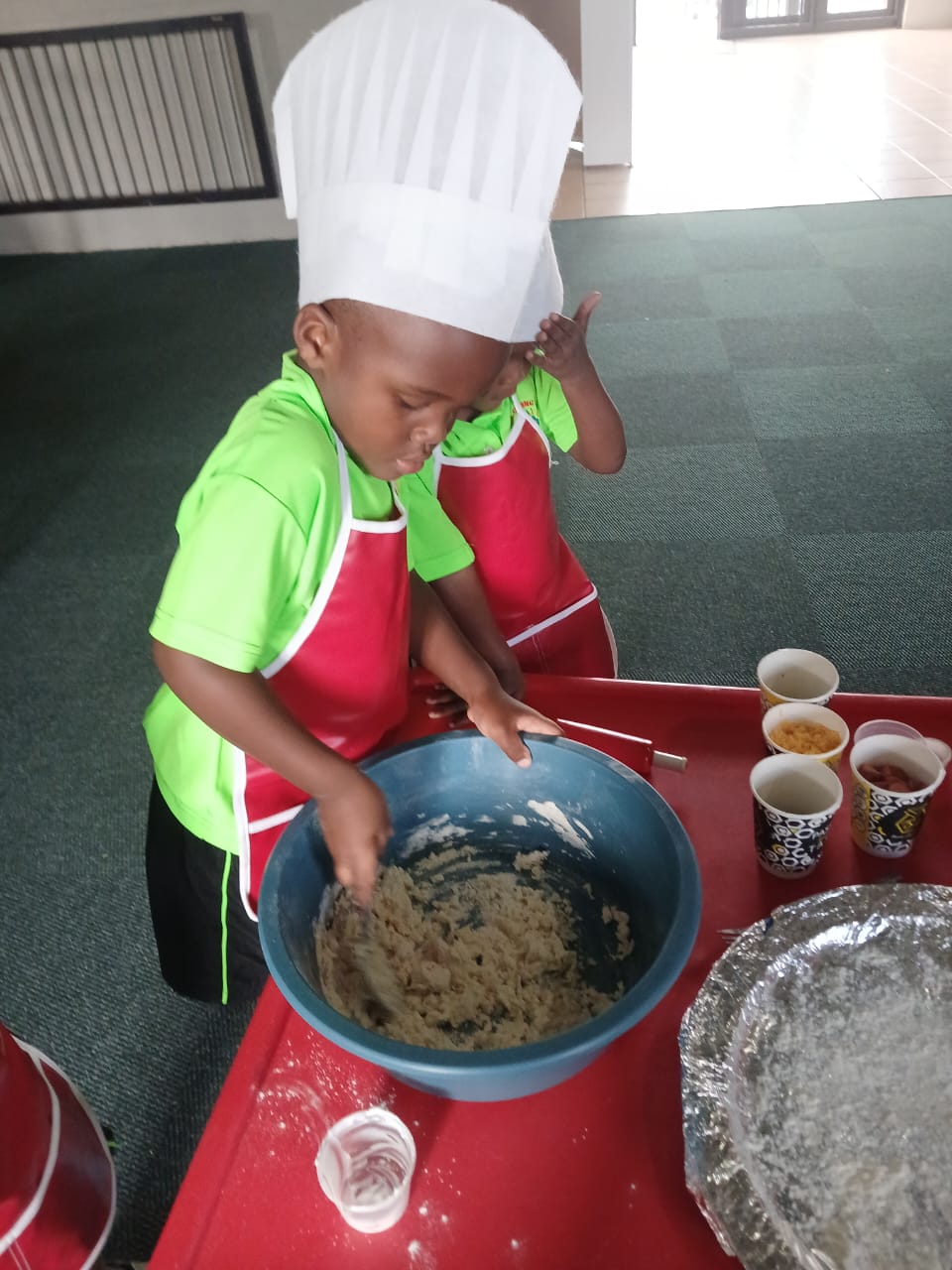 A young child wearing a chef's hat and apron mixing ingredients in a blue bowl during a cooking activity