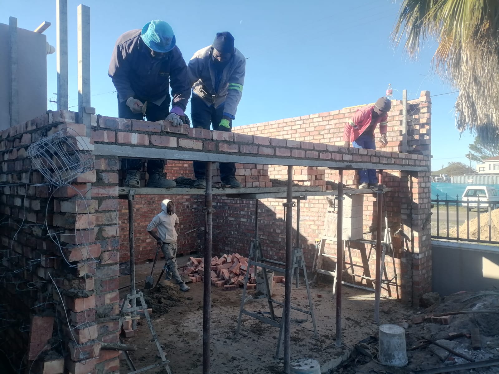 Construction crew building a brick structure with steel roof frame
