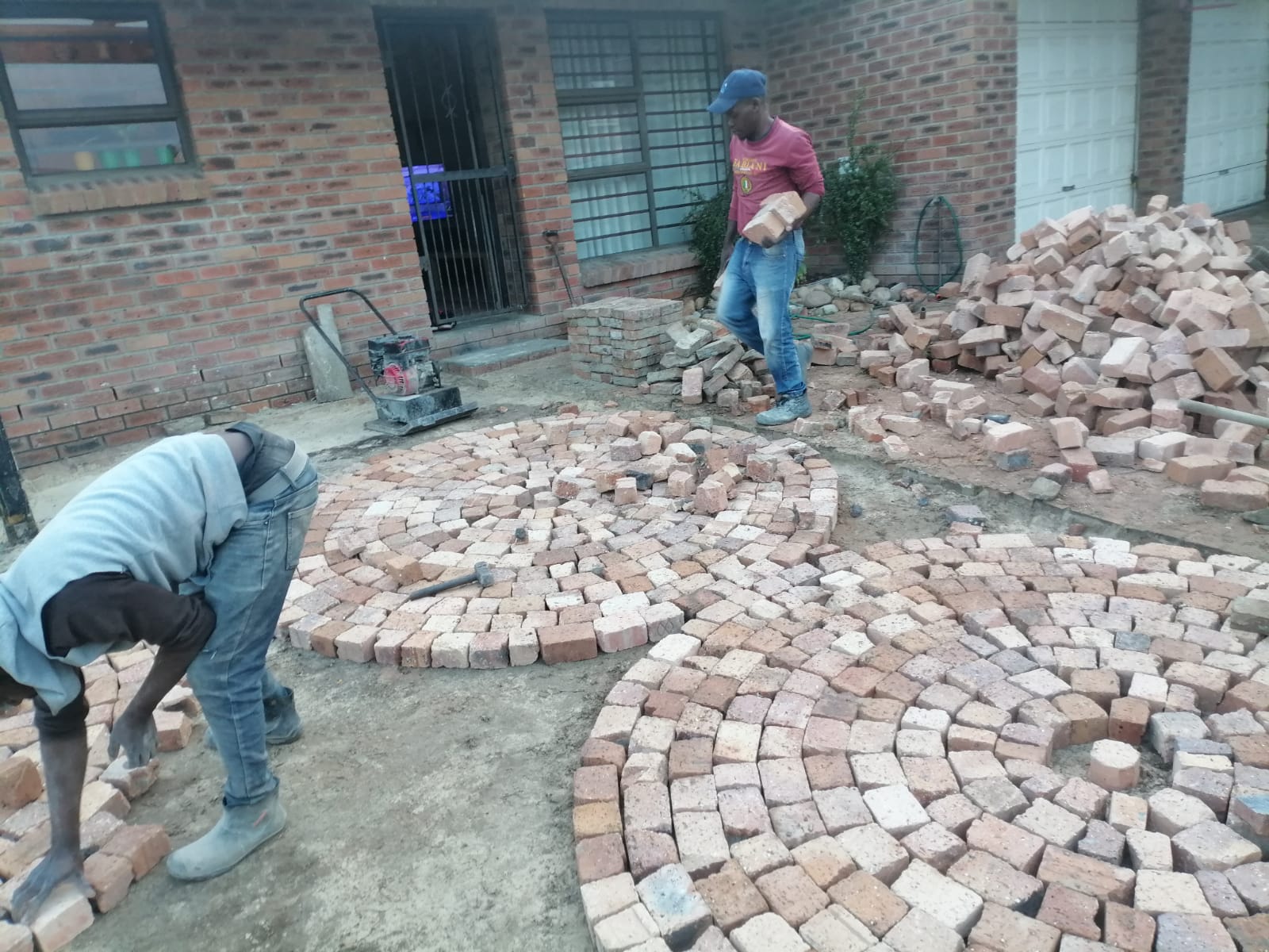 Two workers laying curved brick paving in a courtyard