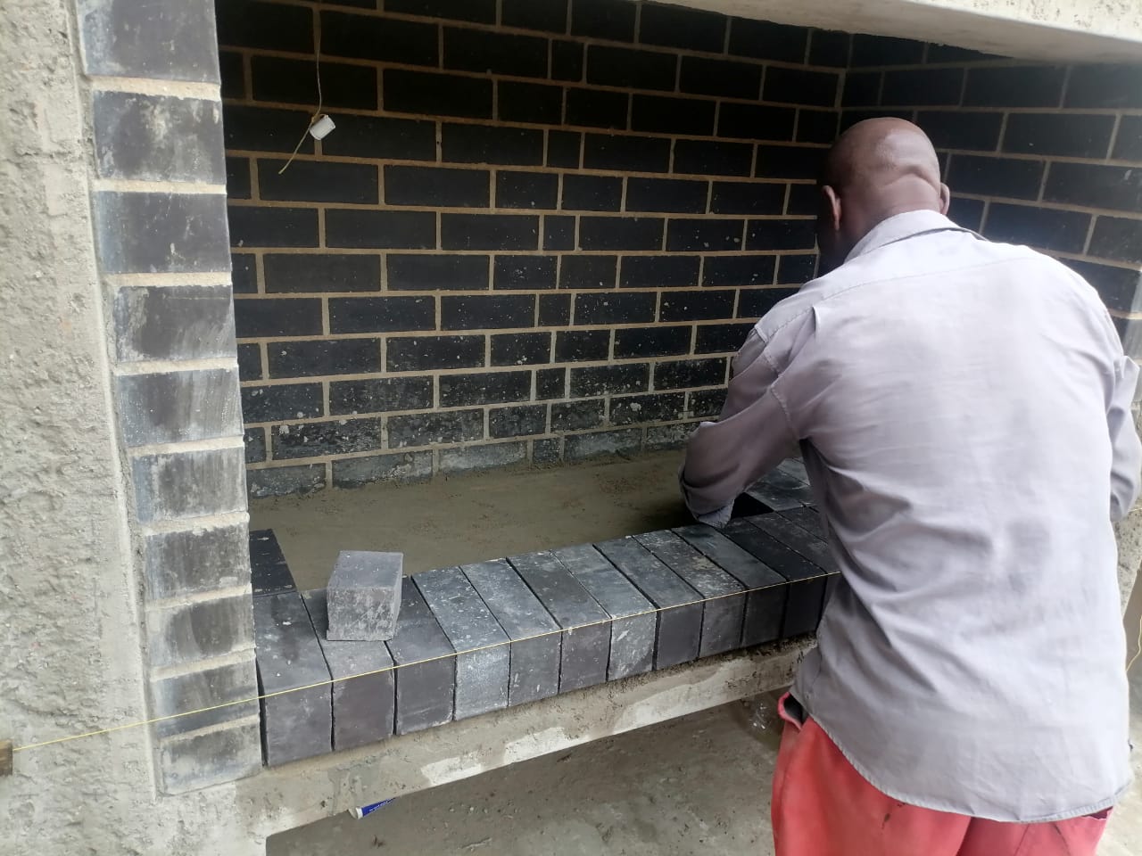 Worker laying dark paving stones along a brick wall